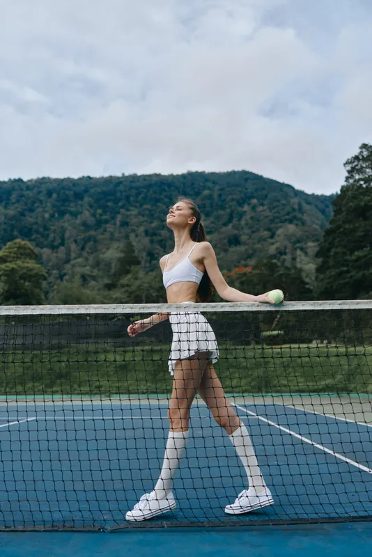 Young female tennis player smiling on the court, showcasing athletic wear and a confident pose against a natural green background