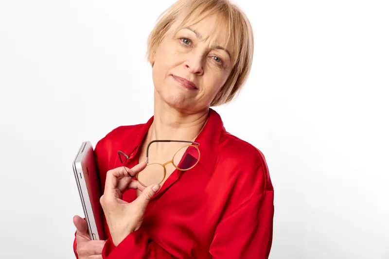 Senior woman nurse holding stethoscope near chest, red medical scrubs, studio portrait on white background, confident smile, healthcare and medical care concept