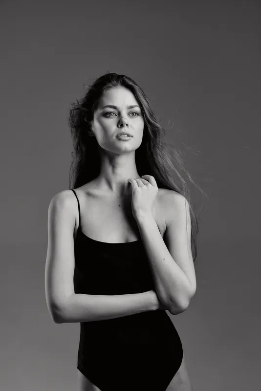 Black and white portrait of a thoughtful woman in a black sleeveless outfit with long hair and serious expression.