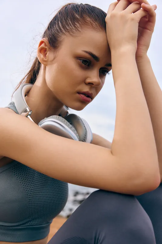 Young athletic female sitting outdoors with headphones, expressing contemplation, wearing sportswear, a perfect representation of healthy lifestyle and self reflection