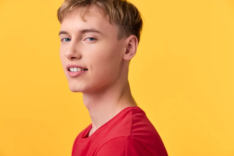 Close up of a smiling boy wearing a red shirt against a vibrant yellow backdrop, conveying youthful energy, cheerful mood, and casual style for lifestyle, fashion, and marketing use
