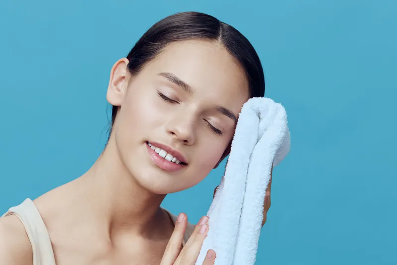 Young woman with a towel, smiling, showcasing beauty and skincare routine against a soft blue background, ideal for wellness and self care concepts