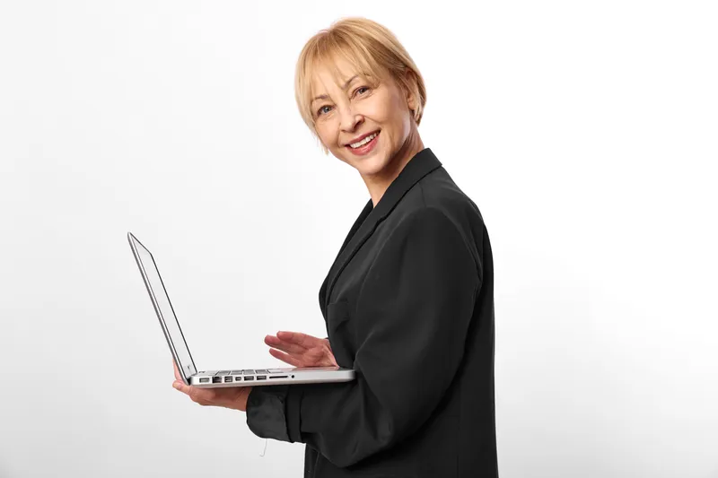 Elderly woman with laptop smile, studio portrait with white background, business attire, technology theme, relaxed pose, soft light, friendly communication, looking at camera, calm