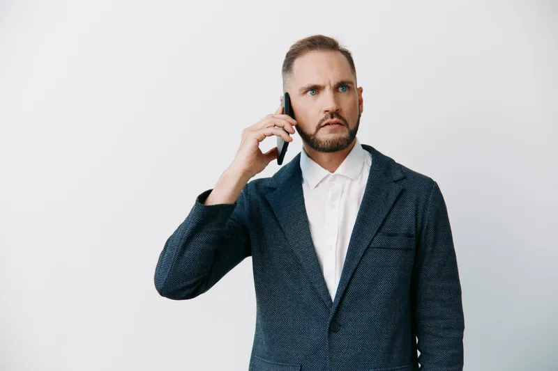 A business professional man on a call, standing against a colored isolated background, expressing focused emotion and determination.