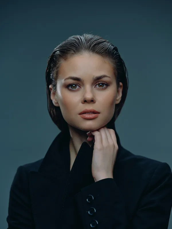 Portrait of a serious woman with dark hair wearing a black coat against a muted background