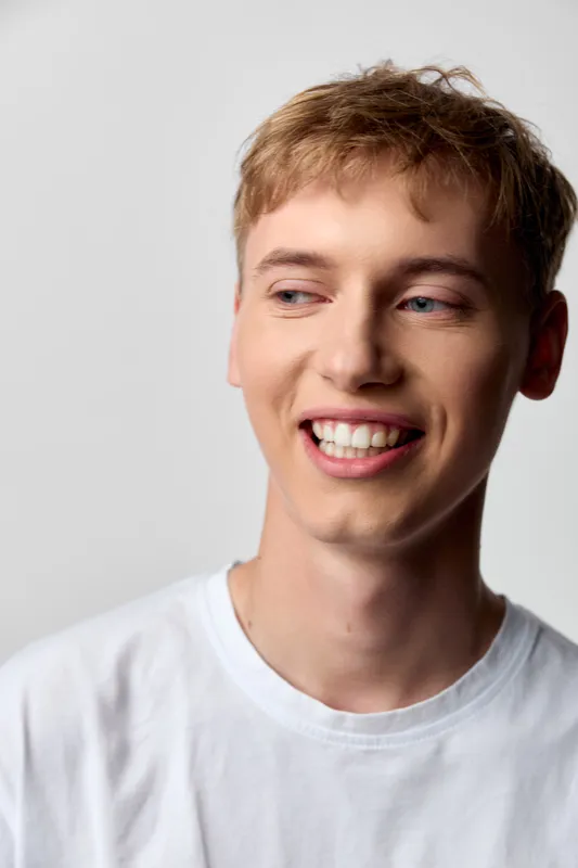 Smiling, young man in a white t shirt exudes friendly charm, open expression and relaxed posture conveying approachable warmth ideal for lifestyle, fashion, wellness, and positive vibes.