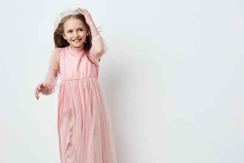 Happy young girl in a pink dress smiling against a neutral background, showcasing joy and innocence, ideal for children s fashion and celebrations