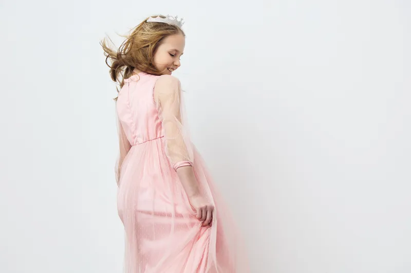 A young girl with flowing hair wearing a delicate pink dress, exuding joy and grace against a soft, neutral background, ideal for themed photography and fashion concepts