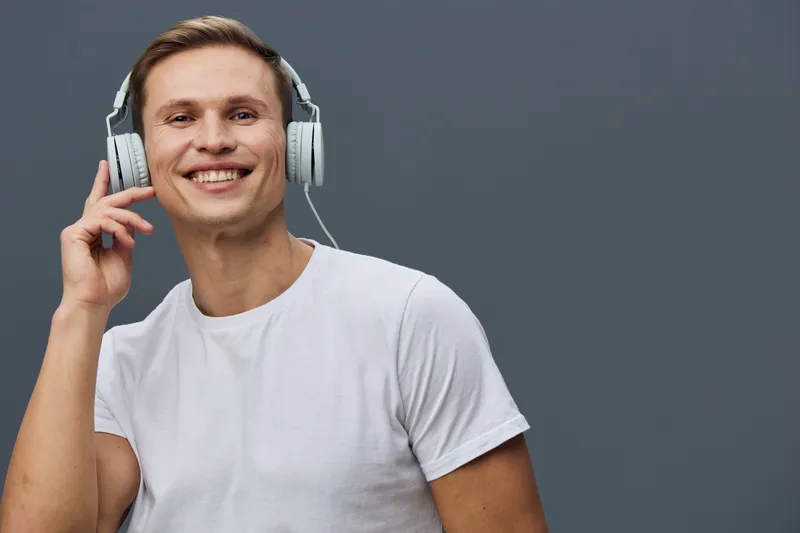 Smiling young man with headphones, casual white t-shirt, listening to music, looking cheerful, studio portrait, lifestyle concept, happy facial expression, modern style, daily life, vibrant emotional 
