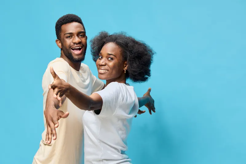 Happy young couple with Afro hairstyles, wearing casual clothes, expressing joy against a blue background, representing love and togetherness