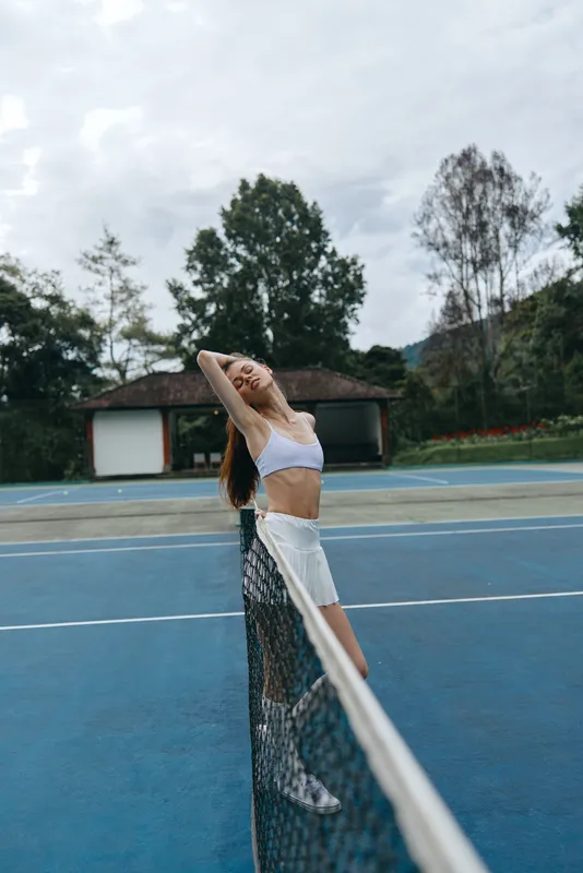 Happy young female tennis player enjoying a moment on the court, wearing sporty attire, showcasing athleticism and confidence against a vibrant outdoor background