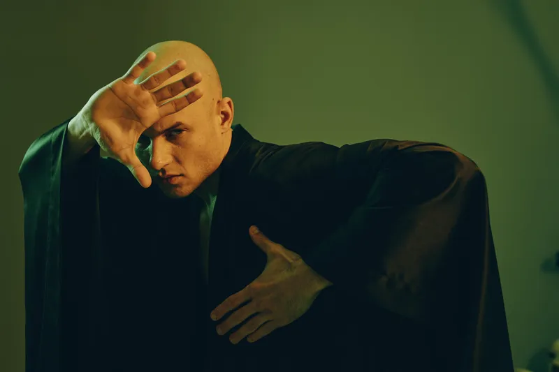 Dramatic man in black attire poses expressively under soft light, showcasing intense emotions and unique artistry, perfect for creative projects and storytelling.