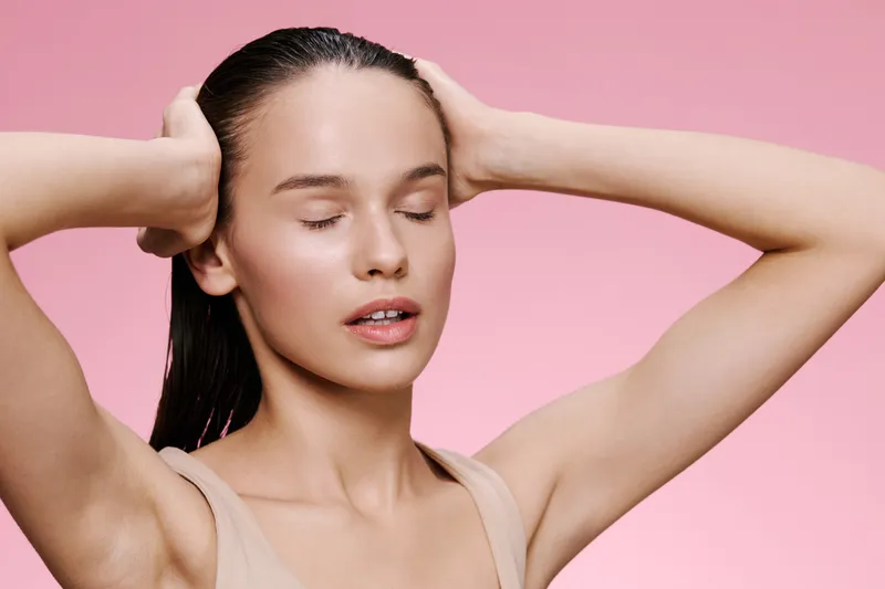 Young woman with closed eyes expressing serenity, wearing a nude top with long hair, against a soft pink background, ideal for wellness and beauty concepts