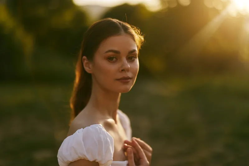 Young woman in a white dress during golden hour, showcasing serene emotions in a lush green outdoor setting, symbolizing beauty and nature