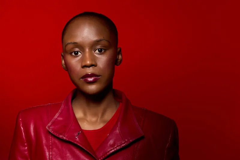 Portrait of a confident black African woman with dark skin wearing a red leather jacket and red shirt against a vibrant red background. Concept of fashion, beauty, and empowerment.