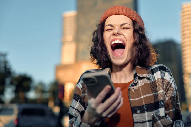 Woman phone scream joy in urban street, candid authenticity and golden hour glow, emotional storytelling and mindful living vibe, modern city lifestyle portrait full of energy.