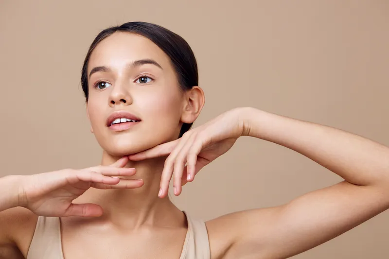 Young female model with natural beauty poses gracefully against a neutral background, showcasing healthy skin, elegance, and serenity in her expression
