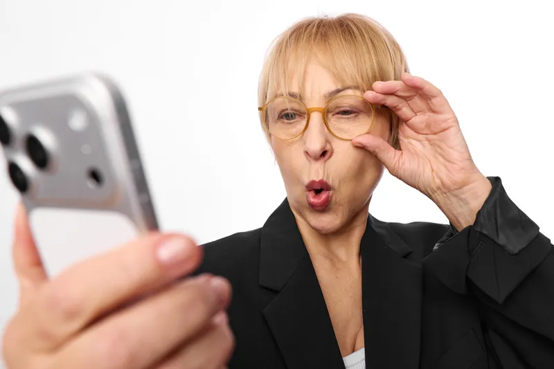 Woman smartphone surprise glasses senior business phone hand concern communication: business senior shocked at phone screen, touches forehead, portrait, isolated white background.