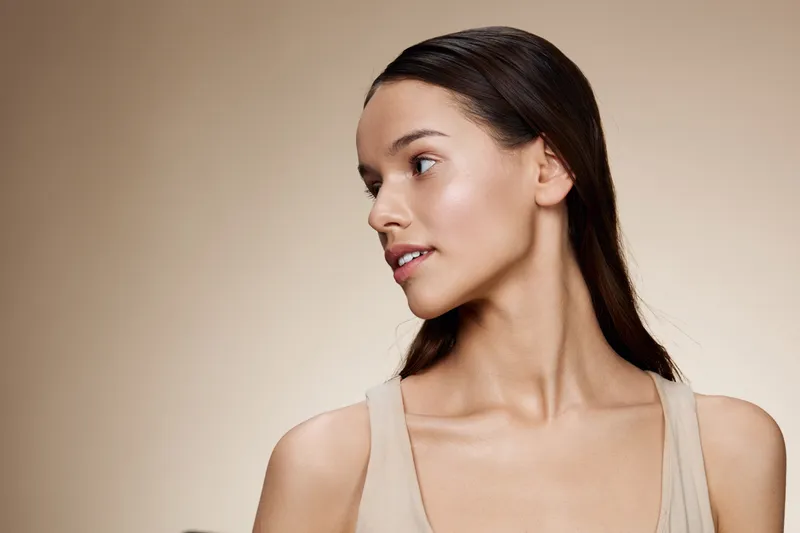 Natural beauty portrait of an elegant young woman, showcasing healthy skin and graceful posture against a soft beige background, perfect for beauty and skincare concepts