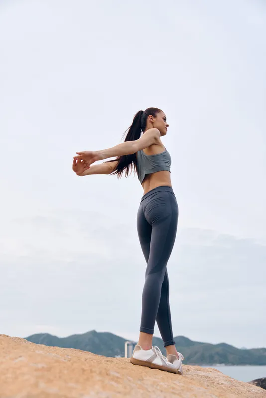 Fit young woman in athletic wear stretching outdoors by the beach, exuding confidence and vitality, perfect for healthy lifestyle concepts