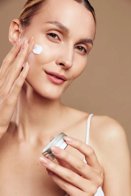 Woman skincare, face cream, applying on cheek, holding jar, beauty routine, moisturized skin, healthy glow, close up portrait, spa treatment, neutral background