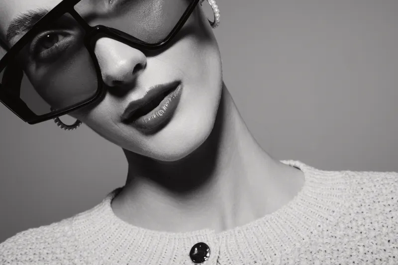 Close-up portrait of a white woman with light skin wearing large sunglasses and a light knitted sweater. Fashion and style concept with minimalistic monochrome aesthetics.