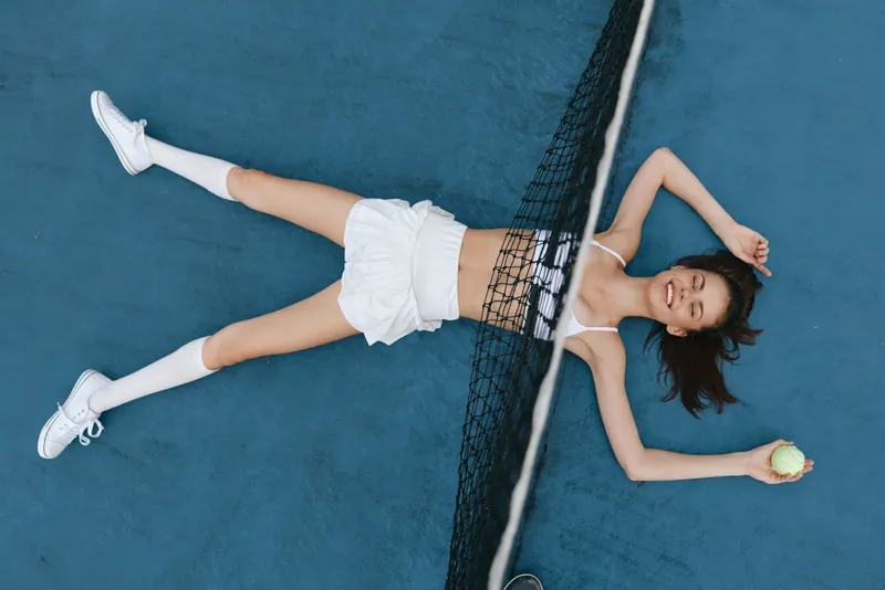 Young female athlete in activewear enjoying a moment of relaxation on a tennis court, showcasing a vibrant and sporty vibe with a bright color palette