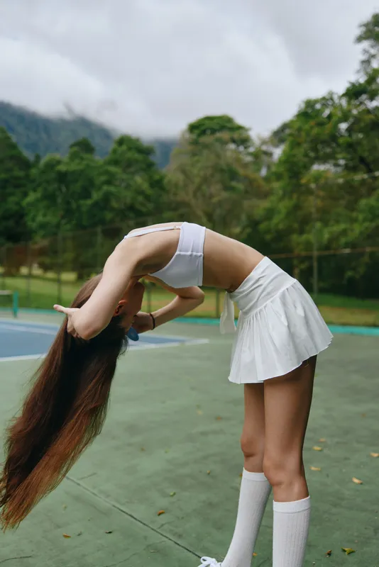 Young athletic woman in a sports outfit performing a playful hair flip outdoors, showcasing energy and grace against a green landscape background