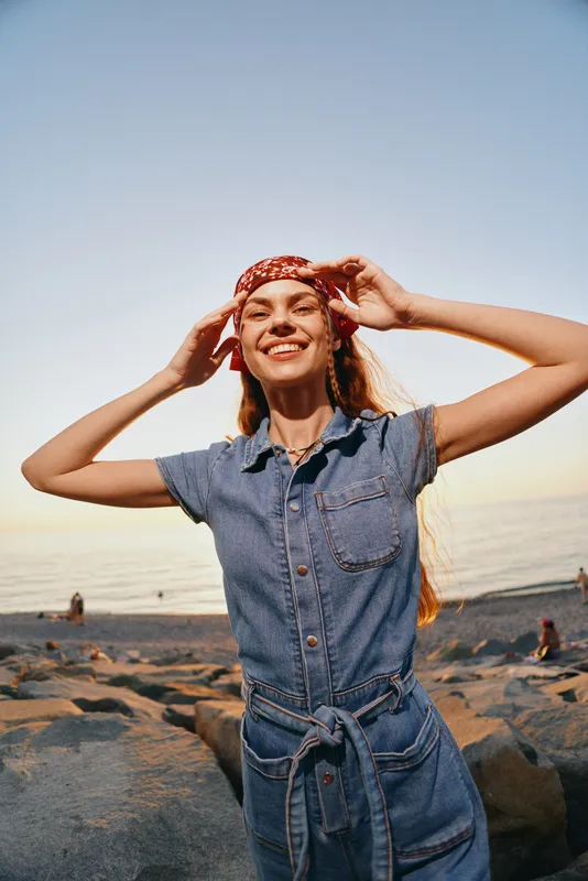 lifestyle woman in modern boho-western denim street style smiling on the beach during golden hour with film color tones and relaxed summer vibe
