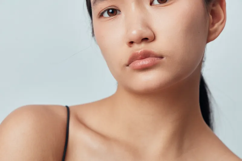 Young woman with natural skin closeup portrait, minimal makeup and black tank top against light background. Calm expression, beauty and skincare concept with clean look and soft lighting.