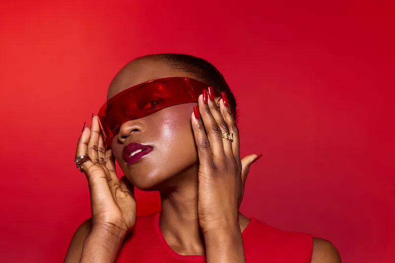 Portrait of a confident dark skinned African woman with shaved head wearing red visor and matching red top against vibrant red background. Concept of fashion, beauty, and bold style.