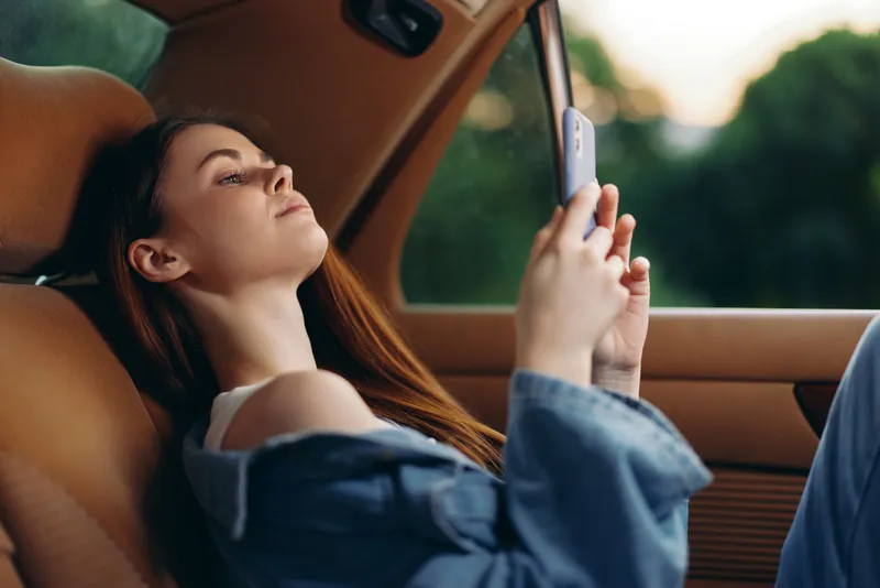 Young woman enjoying a moment of relaxation in a car, using a smartphone, dressed casually in denim, exuding a calm and serene emotion, with a green background.