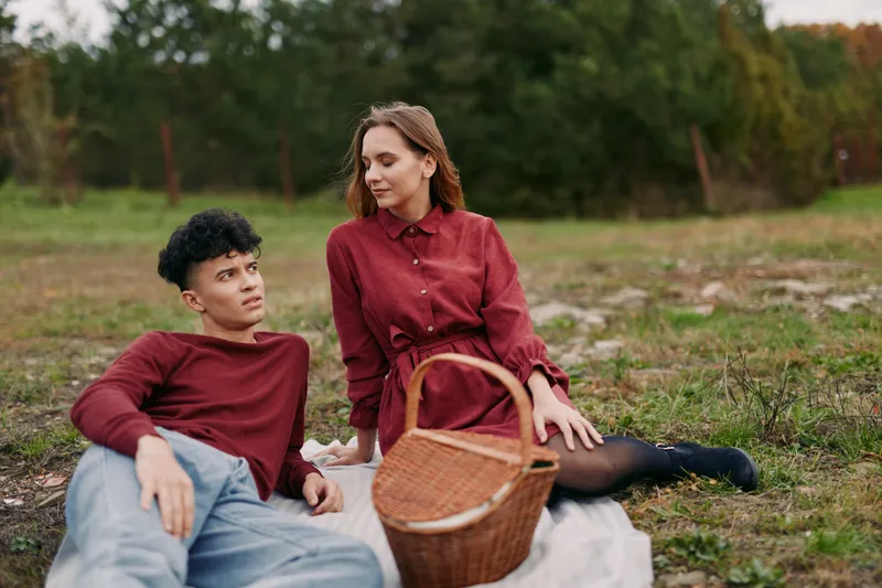 A young couple enjoys a relaxed picnic on a blanket in a grassy field, sharing candid expressions and gentle conversation that convey natural authenticity and quiet credibility.