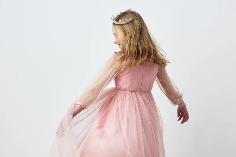 Cute young girl in a pink tulle dress turning around with flowing fabric, capturing a joyful moment against a soft white background Perfect for children s fashion themes