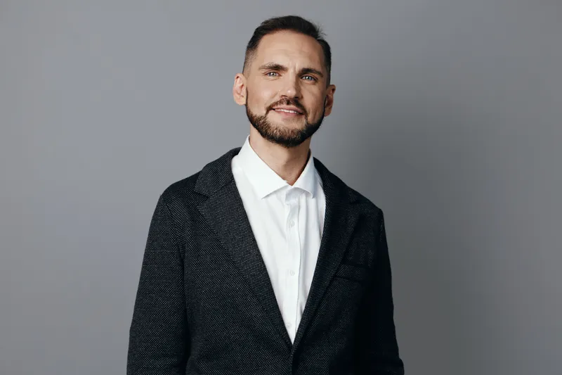 A confident business professional man stands against an isolated colored background, exuding poise, focus, and calm energy with a subtle approachable smile.