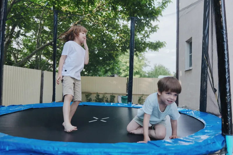Playful boys enjoying fun on a trampoline, laughing and having a great time together in a sunny backyard setting with greenery around.