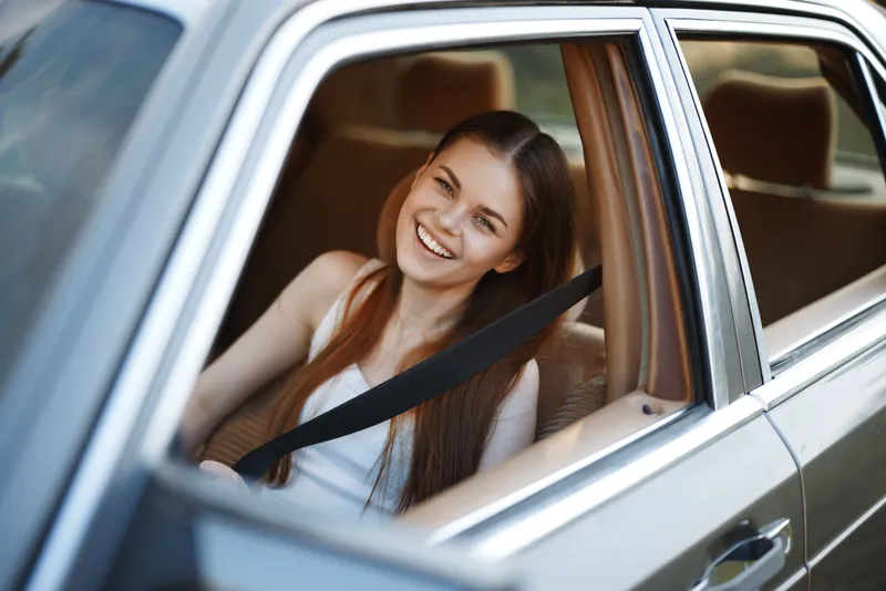 Happy young woman smiling from a car window, showcasing carefree emotions and a relaxed summer vibe, perfect for travel and adventure concepts.