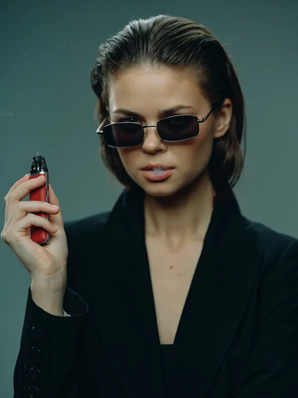 Stylish woman wearing sunglasses holding a red vape device, dressed in black, confident expression, modern fashion accessory