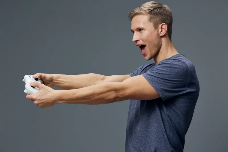 Enthusiastic man holding white game controller playing video games gaming entertainment on gray background digital content generation concept
