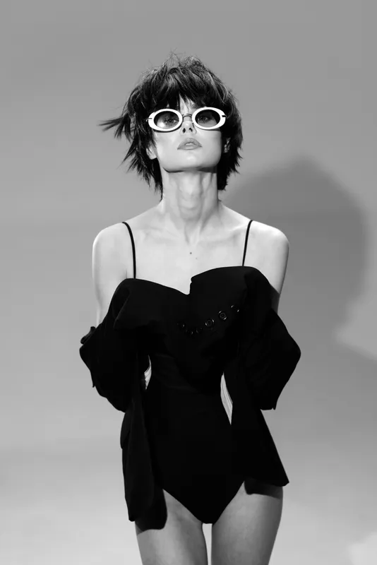 Black and white portrait of stylish woman wearing sunglasses and black outfit with confident pose.