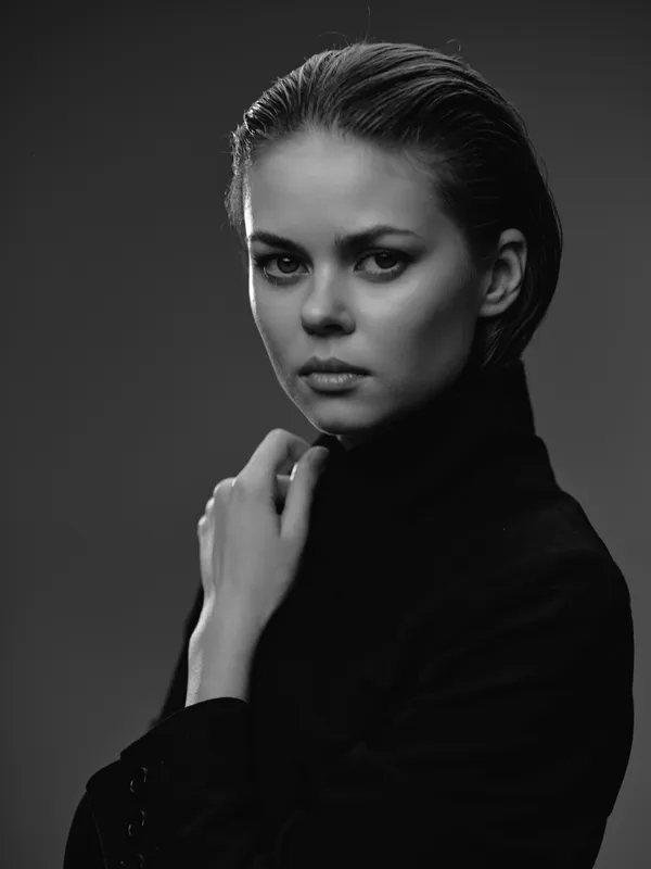 Black and white portrait of a serious woman in dark clothing with slicked-back hair and a thoughtful expression