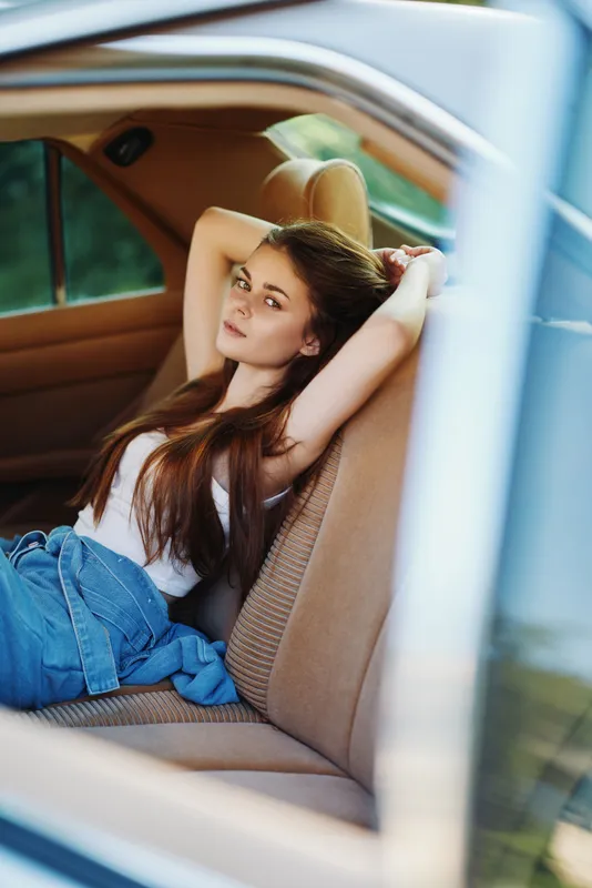 Young woman relaxing in a stylish car interior, showcasing natural beauty and casual fashion with denim and a tank top.