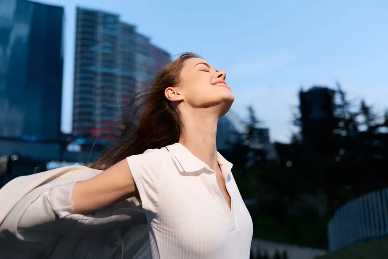 Woman enjoying freedom outdoors with arms outstretched in casual white shirt during sunset urban background lifestyle positivity KEY: woman freedom outdoors casual white shirt arms outstretched positi