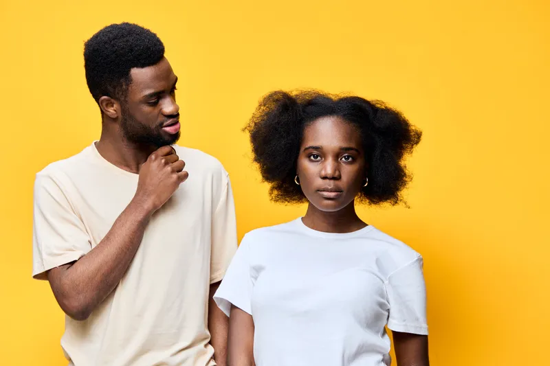 Young Black couple with playful expressions against a vibrant yellow background, showcasing modern casual fashion, conveying emotions of connection and joy
