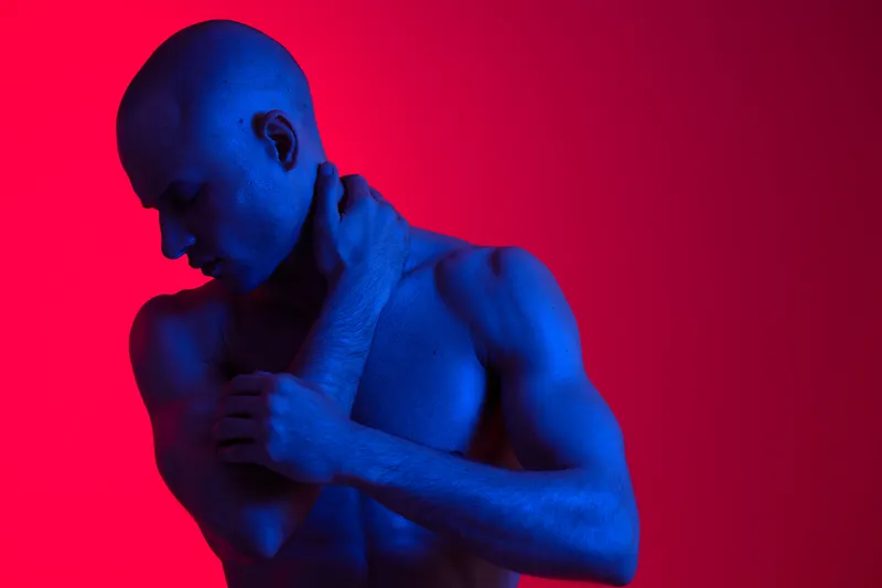 Artistic portrait of a man with dramatic lighting, showcasing strong contrasts and vivid colors. This image emphasizes emotion and physical expression, captivating the viewer.