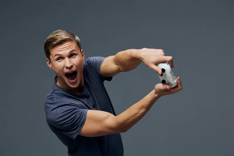 excited young caucasian man holding game controller playing video game isolated on dark background digital entertainment concept