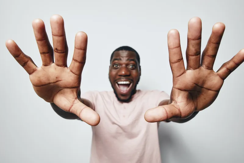 African American man with dark skin smiling and showing open hands to camera, expressing excitement and joy on white background. Casual clothing and positive emotion.