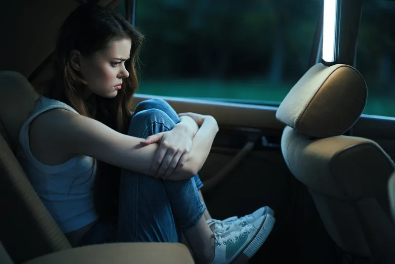 A teenage girl with long hair sitting in a car, reflecting deep emotions while dressed in casual attire, capturing a moment of introspection.