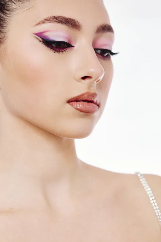 Close-up of a young woman with creative purple eye makeup and bold cat eyeliner. Her lips have a soft brown matte finish. Concept for beauty, fashion, and artistic styling.
