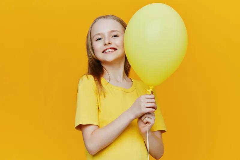 Happy girl holding a yellow balloon against a bright yellow background, wearing a casual yellow t shirt, conveying joy and playful energy